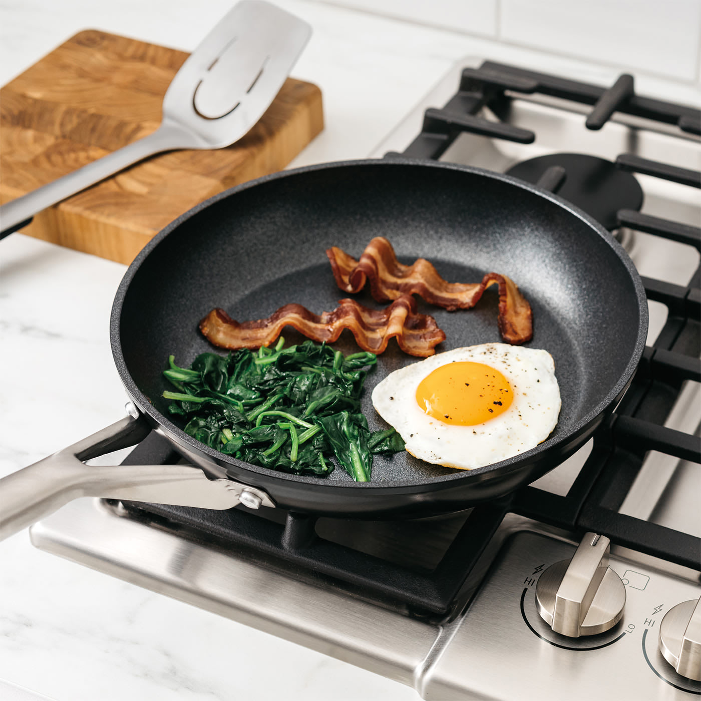 Image of Ninja Frying pan on a gas hob with bacon, spinach, and a fried egg.